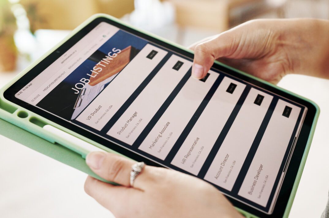 Hands holding a tablet showing a search for job listings.
