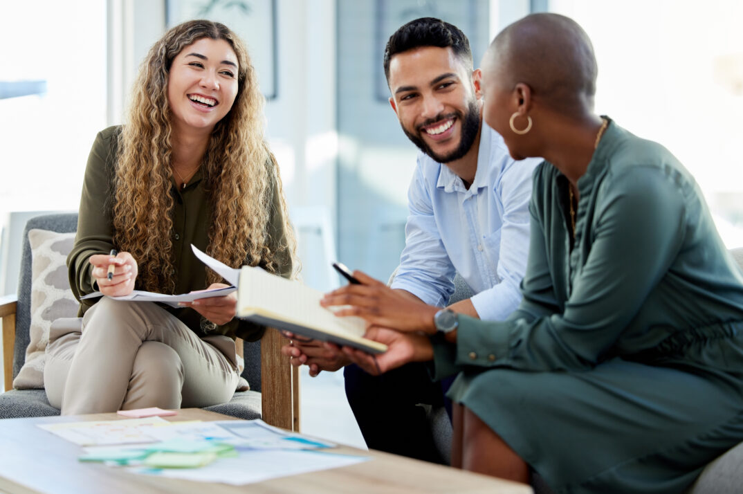 A group of colleagues laugh and chat on office couches.