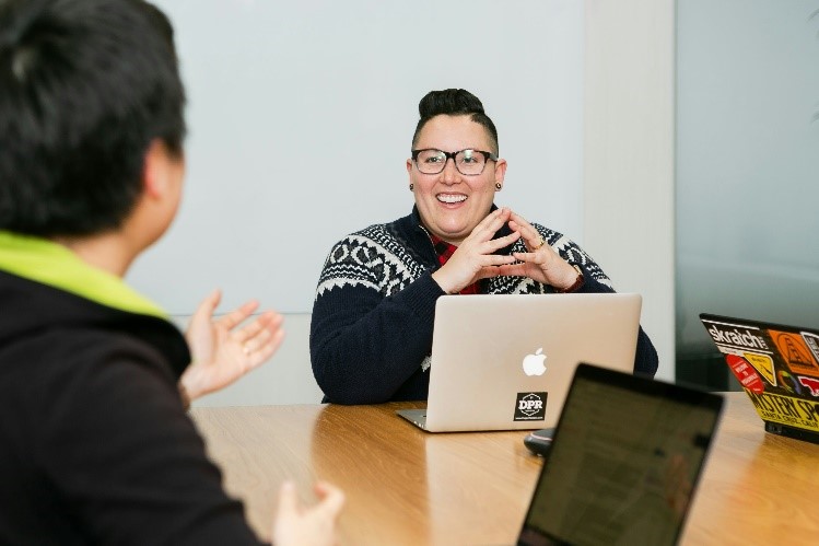 Two people sit at laptops, chatting and smiling at each other.